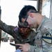 Two U.S. Army soldiers in MultiCam/OCP camouflage uniforms are reviewing paperwork together, with one soldier holding a mobile device while referencing a stack of documents. The foreground soldier wears a 1st Cavalry Division shoulder sleeve insignia and a 'U.S. ARMY' tape. They appear to be conducting administrative or logistical work in what looks like a loading dock or vehicle bay area.