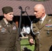 Two military officers in olive/khaki dress uniforms are engaged in conversation outdoors near a building. The officer on the left wears a U.S. Army uniform with a garrison cap and name tape reading 'SAXON', while the officer on the right wears what appears to be a Polish Army uniform with two-star rank insignia and a name tape reading 'WOJCK'. Both display multiple service ribbons and decorations.
