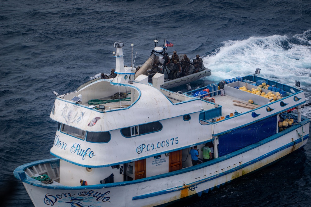 An aerial photograph shows a white and blue fishing vessel named 'Don Rufo' with registration number P.04.00875 being approached or boarded by armed personnel in tactical gear arriving via a rigid inflatable boat (RIB) flying a U.S. flag. The vessel's deck is loaded with yellow buoys, blue barrels, and other cargo. This appears to be a maritime law enforcement or interdiction operation.