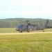 A U.S. Army UH-60 Black Hawk helicopter configured as a medevac (medical evacuation) aircraft is on or near a dirt landing strip in a grassy field. The helicopter displays red cross markings on its fuselage, indicating its medical role. The setting appears to be a military training area surrounded by dense tree lines.