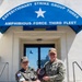 Two military officers are posing for a photo outside the headquarters of Expeditionary Strike Group Three, Amphibious Force Third Fleet. They are jointly holding a commemorative plaque while shaking hands, suggesting an official exchange or visit ceremony. One officer wears a Republic of Korea (ROK) military uniform and the other wears a U.S. Navy uniform.