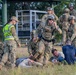 This image depicts a military training exercise involving U.S. Air Force Security Forces personnel responding to a simulated mass casualty or active threat scenario. Several uniformed personnel in OCP (Operational Camouflage Pattern) are attending to role-playing casualties on the ground, with one wearing a high-visibility 'POLICE' vest. The scene includes tactical gear, helmets, body armor, and radio communications consistent with a realistic training drill.