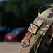 Close-up photograph of a military uniform sleeve showing unit patches on an OCP (Operational Camouflage Pattern) uniform. The patches identify the wearer as a Security Forces (SF) member of the Air National Guard. A radio antenna is visible over the shoulder, and blurred vehicles and trees appear in the background.