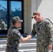 Two military personnel are shaking hands outside a building at what appears to be a naval installation. One individual wears a Republic of Korea (ROK) Army uniform with a South Korean flag patch, while the other wears a U.S. Navy uniform with a single star insignia indicating the rank of Rear Admiral (Lower Half). A naval vessel is visible in the background through the glass doors.