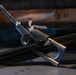 A close-up photograph of metal rigging or tensioning hardware, likely turnbuckles or similar fastening devices, resting on a flat surface alongside green nylon webbing straps and rope. The metal components show signs of wear and use, with knurled grips and clevis-style end fittings visible. The image appears to depict equipment used in sailing, rigging, or load-securing applications.