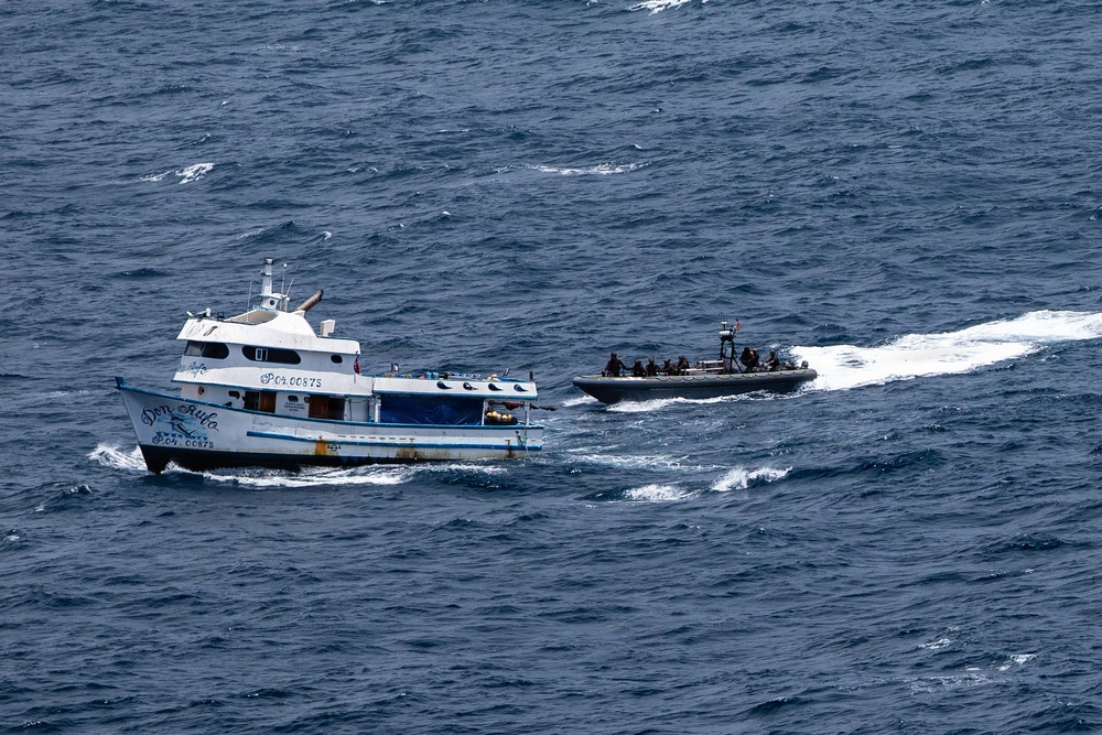 An aerial photograph shows two vessels at sea: a white and blue civilian-style motor yacht named 'Don Rulo' with registration number PC.04.00875, being approached by a rigid inflatable boat (RIB) carrying multiple personnel in dark tactical gear. The RIB appears to be conducting an intercept or boarding operation alongside the larger vessel. The scene is consistent with a maritime law enforcement or interdiction operation.