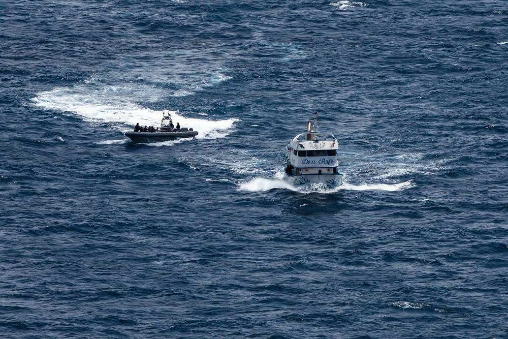 An aerial photograph shows two vessels on open ocean waters. A white civilian motor yacht named 'Don Rufo' is being approached or intercepted by a rigid inflatable boat (RIB) carrying multiple personnel in dark clothing. The scene suggests a maritime law enforcement or interdiction operation.