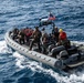 A rigid-hull inflatable boat (RHIB) marked '11MRX 1001' is underway on open ocean waters carrying multiple military personnel. The boat flies a United States flag and is equipped with a mast-mounted sensor or camera system. Personnel aboard are wearing a mix of tactical gear, life vests, and helmets, suggesting a military training or operational mission.