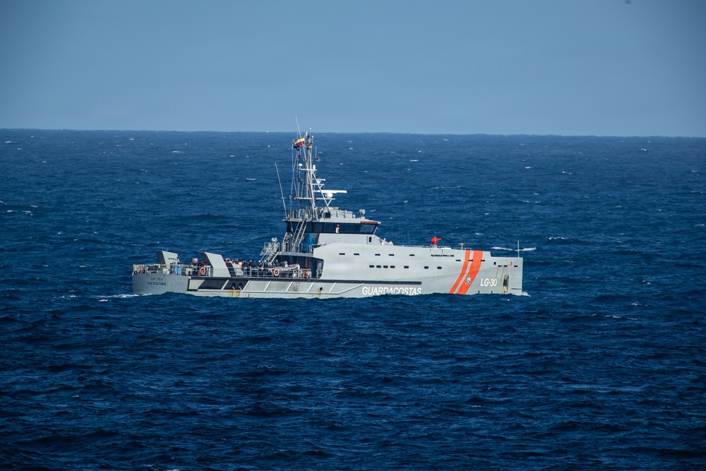 A Venezuelan Coast Guard patrol vessel designated LG-30 is underway on open ocean waters. The gray-hulled ship bears the name 'GUARDACOSTAS' on its hull along with distinctive orange diagonal stripes, and flies what appears to be a Venezuelan flag from its mast. The vessel appears to be on active patrol duty in moderately choppy blue seas.