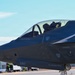 A close-up photograph of an F-35 Lightning II stealth fighter jet on a taxiway or flight line. The aircraft bears the tail number 5817 and is marked with the name 'COL STEPHEN PIERCE' below the cockpit. A pilot wearing a flight helmet is visible seated in the single-seat cockpit.