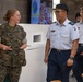 A U.S. Marine in woodland MARPAT camouflage uniform is engaged in conversation with military personnel wearing light blue and navy dress uniforms, likely from an Asian air force. The interaction appears friendly and informal, possibly during a joint military exchange or liaison event. The setting appears to be an indoor facility, possibly a dining facility or common area.