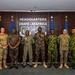 A group of nine military personnel pose for a formal photograph at Headquarters USAFE-AFAFRICA (United States Air Forces in Europe - Air Forces Africa). The group includes personnel in various military uniforms representing multiple nations, standing in front of the official headquarters signage. Flags including the United States flag, German flag, and Air Force flags are visible in the background.