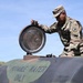 A U.S. Army soldier in OCP (Operational Camouflage Pattern) uniform is opening the hatch of a military potable water tank. The tank is painted olive drab and labeled 'POTABLE WATER ONLY' in stenciled lettering. Solar panels are visible in the background, suggesting a forward operating base or installation with renewable energy infrastructure.