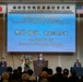 This image shows a formal commemoration ceremony for the return of the Negishi Dependent Housing Area, held at the Sheraton Yokohama Bay Hotel &amp; Towers. Mr. Kuroiwa Yuji, Governor of Kanagawa Prefecture, is delivering a speech at the podium. The event features both Japanese and American flags, indicating a bilateral Japan-U.S. occasion.