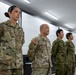 Four military personnel are standing at attention in what appears to be a briefing or conference room. Two individuals wear U.S. Army OCP (Operational Camouflage Pattern) uniforms, while two others wear what appears to be Japan Ground Self-Defense Force (JGSDF) camouflage uniforms. The setting suggests a joint military exercise or bilateral meeting between U.S. and Japanese forces.