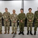 Six military personnel are posed together in what appears to be a briefing or conference room. Three individuals on the left wear U.S. Army OCP (Operational Camouflage Pattern) uniforms, while three on the right wear Japan Ground Self-Defense Force (JGSDF) digital camouflage uniforms. This appears to be a joint military cooperation or exchange event between U.S. Army and Japanese Self-Defense Force personnel.
