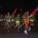 A group of military personnel, likely U.S. Marines, are conducting a formation run at night on a paved road. The runners are wearing olive drab physical training uniforms with reflective safety belts, and the lead runners are carrying red unit guidon flags. The scene appears to be a unit physical training event on a military installation.