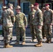 A group of multinational military personnel are gathered outdoors in front of a building, appearing to be engaged in informal conversation. The group includes soldiers wearing different national uniforms and headgear, suggesting a joint military exercise or official meeting. The setting appears to be a military installation, likely in Japan based on visible Japanese signage and Japanese Ground Self-Defense Force personnel present.