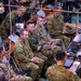 A multinational military command post or operations center showing personnel from multiple nations gathered around long tables equipped with laptops and communications equipment. The scene appears to be a joint military exercise or briefing, with personnel wearing various national uniforms including Australian Army (AUSCAM pattern), US Army (OCP/Multicam), and Japanese Ground Self-Defense Force uniforms. Civilian personnel in suits are also present, suggesting a high-level coordination or liaison event.