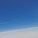A single F-35 Lightning II stealth fighter jet is photographed in flight against a clear blue sky with thin cirrus cloud layers below. The aircraft displays U.S. Air Force markings and tail code 'WI', indicating assignment to a Wisconsin Air National Guard unit. The image is a high-quality air-to-air photograph taken from close proximity, likely from another aircraft.
