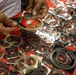 A person is handling United States Marine Corps emblem stickers/decals spread across a red surface. The stickers feature the official USMC Eagle, Globe, and Anchor emblem on a red and gold circular design. Multiple stickers are visible in individual clear plastic packaging, suggesting a distribution or display setting.