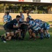 A rugby union match is being played at a ground in the Northern Territory, Australia, as indicated by the 'Friends of Rugby Northern Territory' signage. Two teams are engaged in a ruck or maul contest near the center of the field, with one team wearing black and the other in blue-and-white hooped jerseys. The match is taking place at an established club ground featuring a covered grandstand labeled the 'OneSteel Stand'.