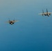 Four military jet aircraft are flying in a loose formation against a clear blue sky. The formation consists of two distinct aircraft types: two F-35 Lightning II stealth fighters on the left and two F-15 Eagle fighters on the right. The image appears to be an aerial photograph taken from another aircraft at a similar altitude.