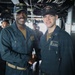 Two U.S. Navy sailors are shaking hands aboard what appears to be the bridge or interior of USS John Finn (DDG-113), a guided-missile destroyer. The sailor on the right wears a name tag reading 'J.A. Zumwalt' and is assigned to 'ER Division,' while both wear USS John Finn DDG-113 caps. Several other crew members are visible in the background, suggesting a formal recognition or ceremony moment.