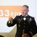 A U.S. Army officer in dress uniform (Army Service Uniform with bow tie, indicating a formal military event) is holding up what appears to be small vials or test tubes. His name tag reads 'HOBBS' and he wears the 101st Airborne Division patch along with multiple service ribbons and crossed rifles insignia. The background displays a projection reading '33RD,' suggesting this is likely a military anniversary or formal dining-in/dining-out ceremony.