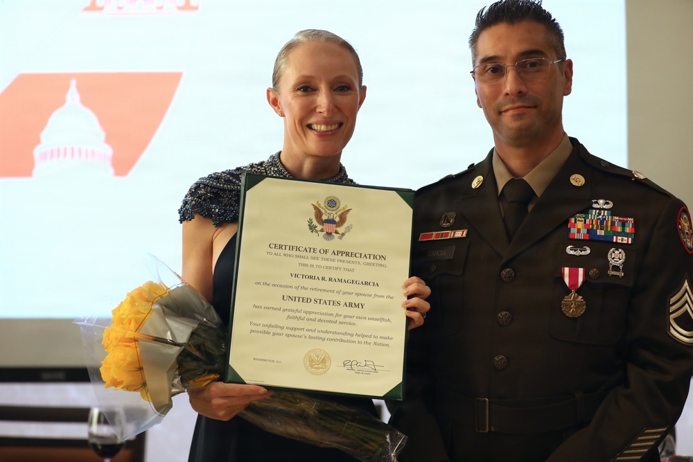 A U.S. Army soldier in dress uniform stands alongside a woman holding a Certificate of Appreciation and yellow flowers. The certificate is issued by the United States Army to Victoria R. Ramagegarcia on the occasion of her spouse's retirement. The setting appears to be a formal military retirement ceremony.
