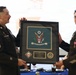 Two U.S. Army soldiers in dress uniforms are presenting a framed award or shadow box during what appears to be a formal military ceremony or banquet. The framed piece features the U.S. Army seal for the 33rd Civil Support Team (WMD) and is dedicated to SFC Daniel A. Garcia. The event is taking place in a banquet hall setting with other attendees visible in the background.