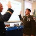 Two U.S. Army soldiers in dress uniforms are conducting a formal oath or re-enlistment ceremony, with both raising their right hands. The event appears to be taking place during a military dining-out ceremony, as indicated by the projected screen reading 'MD-CST's – 2026 Dining Out' and a formally set banquet table in the background. A flag with the number '33' is visible to the right side of the room.