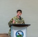 A U.S. Army soldier named Freeland is speaking at a podium during an event at Fort Belvoir. The individual is wearing Army Combat Uniform (ACU) in OCP (Operational Camouflage Pattern) and is gesturing while addressing an audience. The Fort Belvoir seal is visible on the front of the podium.