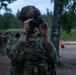 A U.S. Army soldier in full combat gear is adjusting or testing night vision goggles (NVGs) during what appears to be a dusk or low-light training exercise. The soldier wears Operational Camouflage Pattern (OCP) uniform, a tactical helmet with a U.S. flag patch, and a plate carrier vest. Additional soldiers in formation are visible in the background, suggesting a unit-level training event.