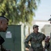 Three U.S. Army soldiers in Operational Camouflage Pattern (OCP) uniforms are engaged in conversation outdoors at what appears to be a military installation. The soldier on the right wears a 'CBRN' (Chemical, Biological, Radiological, and Nuclear) branch tab, and the soldier on the left has a name tape reading 'YAO'. A third soldier stands in the background observing or listening.