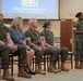 A military briefing or training session titled 'Social Fitness and ACT 101' is taking place on Thursday, 3 September 2026. A female Marine in camouflage uniform is standing and speaking into a microphone while gesturing, addressing a panel of seated individuals that includes both military personnel in MARPAT camouflage and at least one civilian woman. The event appears to be held in a formal meeting or conference hall.
