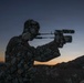 A creative double-exposure or composite photograph blending the silhouette of a person operating a video camera with a rocky, stone-covered landscape. The image is set against a twilight sky with warm orange and cool blue tones near a mountainous horizon. The artistic technique makes the figure appear to be constructed entirely of rocks and stones.