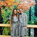 Two individuals wearing matching gray/teal scrubs are posing together and smiling in what appears to be a hospital or medical facility hallway. Both are wearing ID badges, and one has a stethoscope and is wearing a gray Patagonia fleece jacket over her scrubs. They are standing in front of a large decorative mural depicting an autumn forest scene.