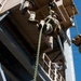 Military personnel in camouflage uniforms are conducting rappelling or fast-rope training exercises from an elevated training tower structure. Multiple soldiers are visible at various stages of descending ropes, while an instructor in civilian clothing observes from a lower platform. The image is taken from a low angle looking upward, emphasizing the height and dynamic nature of the training activity.