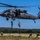TACP Airmen master vertical infiltration A United States Army UH-60 Black Hawk helicopter hovers low over an open field while soldiers conduct fast-rope insertion/extraction (FRIES) training. Multiple soldiers are actively rappelling down ropes from the aircraft while others have already landed and are moving away on the ground. The setting appears to be a military training area with open grassland and tree lines in the background.