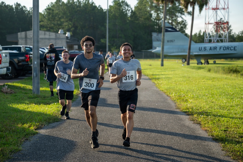 A group of runners participate in an organized race on a paved path at what appears to be a U.S. Air Force base. The foreground features two lead runners wearing bibs numbered 300 and 316, with additional runners visible behind them. A static display aircraft marked 'U.S. AIR FORCE' is prominently visible on the grassy area to the right.