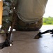 The image shows military personnel in camouflage uniforms (OCP/MultiCam pattern) kneeling on a concrete surface near an edge or opening. Two anchor points or rappelling anchor holes are visible in the concrete floor, with ropes or cordage threaded through them. The setting appears to be an elevated platform or rooftop used for rappelling or rope descent training.