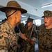 A U.S. Marine drill instructor wearing a campaign cover (drill sergeant hat) is confronting or instructing a recruit in MARPAT camouflage utilities. The scene appears to take place in an indoor training facility with multiple other Marines visible in the background. This is consistent with a military basic training or recruit depot environment.