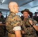 A U.S. Marine drill instructor wearing a campaign cover (drill sergeant hat) is confronting a recruit in what appears to be a barracks setting. The drill instructor is grabbing the recruit's collar and appears to be yelling, a classic training scenario during Marine Corps boot camp. Multiple other recruits and personnel are visible in the background.