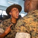 A U.S. Marine drill instructor wearing a distinctive campaign cover (drill sergeant hat) is shouting directly at a recruit during what appears to be a military training or boot camp scenario. The drill instructor is visibly sweating and gesturing with a pointed finger toward the recruit's chest. Additional Marines in MARPAT camouflage uniforms are visible in the background.