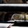 U.S. Marines with 3rd LCT participate in a live-fire basic skills package A person wearing military or tactical gear, including a helmet and protective eyewear/goggles, is visible through a narrow gap between vehicle panels or armor plating. The image is taken from outside a military-style vehicle, looking through what appears to be a window or hatch opening. The composition creates a framed, confined view of the individual inside.