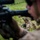U.S. Marines with 3rd LCT participate in a live-fire basic skills package The image shows military personnel in tactical field positions on a grassy terrain, likely during a training exercise. Soldiers wearing desert camouflage uniforms and tactical helmets with mounted equipment are positioned low in the grass. The foreground features a soldier aiming a rifle, with additional personnel visible in the middle ground.