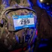 A close-up photograph of a military camouflage backpack bearing a race bib attached to its exterior. The bib is from the 2026 Royal Danish Air Force Flyer March event held at Kadena AB on 29 August 2026, assigned to participant 'Beard' with bib number 795 for the 20 KM distance. The backpack is marked with 'U.S.' indicating it belongs to a U.S. military service member.