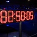 A large LED digital timer/clock display is mounted on a pole stand, photographed at night during what appears to be an outdoor event. The display shows red LED digits reading approximately '88:60:08' or a similar time format, though some digits may be mid-transition. The background shows a dark outdoor environment with scattered colored lights in the bokeh.