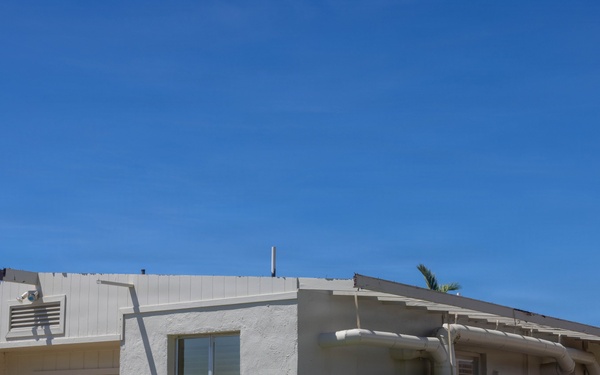 A single-story, white stucco building numbered '278' photographed under a clear blue sky. The structure appears to be a utilitarian or institutional building, possibly located on a military base or government facility, featuring minimal architectural ornamentation and visible HVAC equipment. The surrounding grounds are well-maintained with trimmed grass and a concrete walkway.